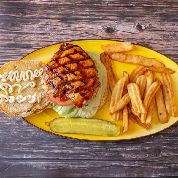 Grilled chicken sandwich with lettuce, tomato, and mayonnaise, served with fries and a pickle.