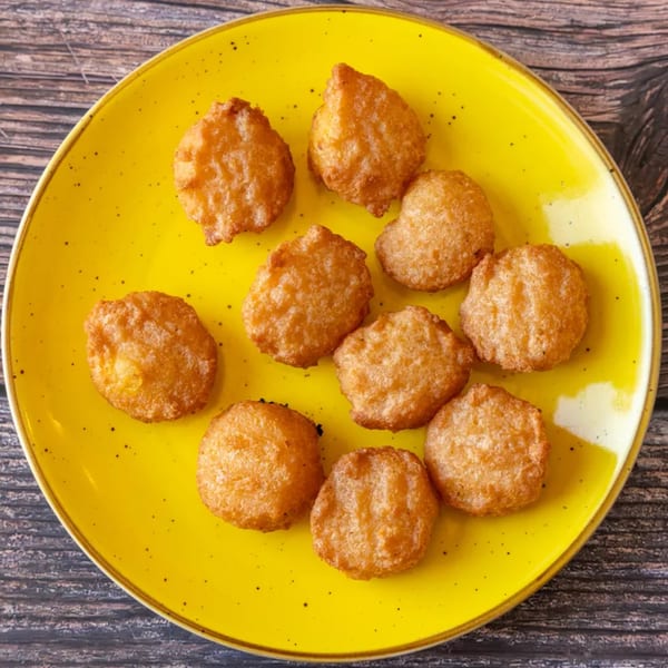 Golden-brown fried hushpuppies or fritters arranged on a bright yellow plate on a wooden table.