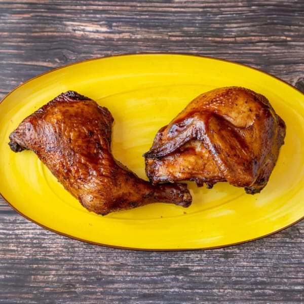 Two pieces of roasted chicken, a leg and a thigh, on a bright yellow oval plate.