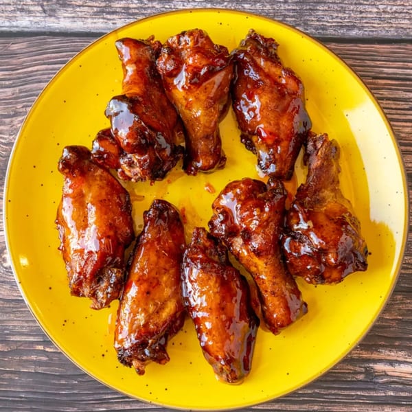 Eight glossy, dark brown chicken wings with sauce on a bright yellow plate.
