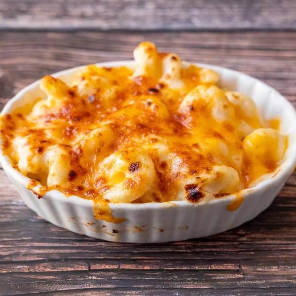 Baked macaroni and cheese in a white ramekin, with a golden-brown crust, on a wooden table.