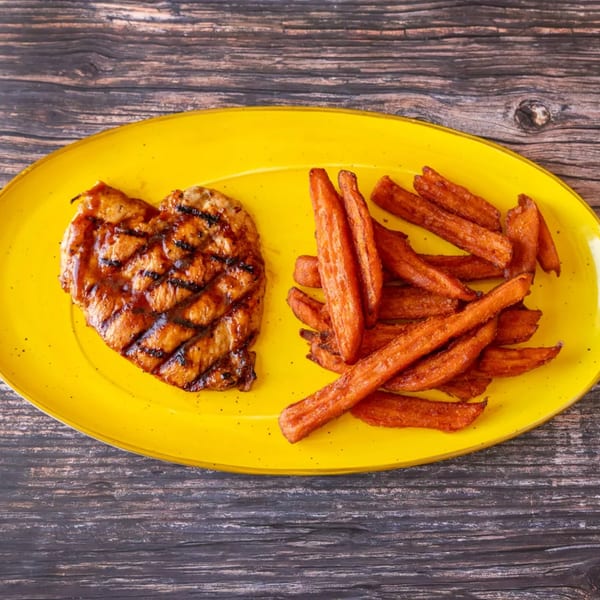 Grilled chicken breast with grill marks and a side of sweet potato fries on a yellow plate.