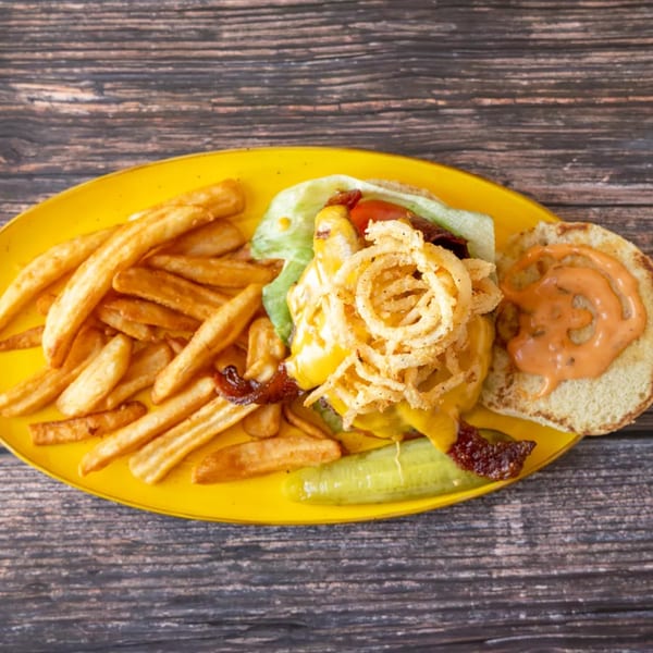 A cheeseburger with onion rings, bacon, lettuce, tomato, and a side of fries and a pickle.