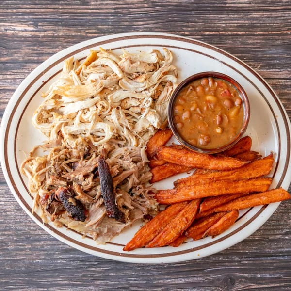 A plate of shredded chicken, pulled pork, sweet potato fries, and a side of baked beans.